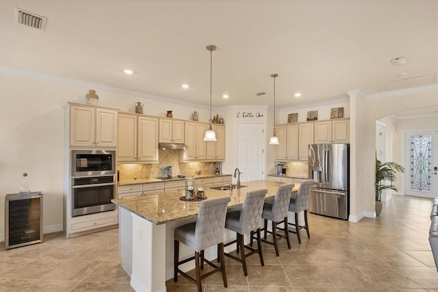 kitchen featuring light stone countertops, stainless steel appliances, wine cooler, an island with sink, and a breakfast bar area