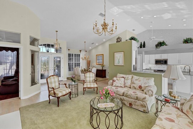 living room with french doors, ceiling fan with notable chandelier, sink, light hardwood / wood-style flooring, and high vaulted ceiling