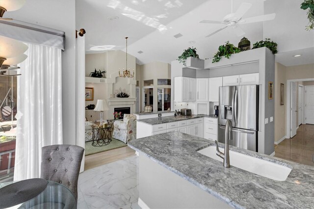 kitchen with pendant lighting, vaulted ceiling, stainless steel fridge, light stone counters, and white cabinetry