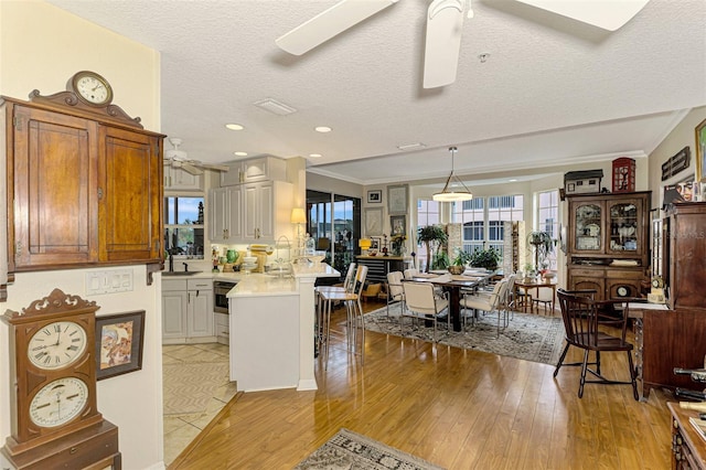 kitchen with a textured ceiling, light hardwood / wood-style floors, white cabinetry, and ceiling fan