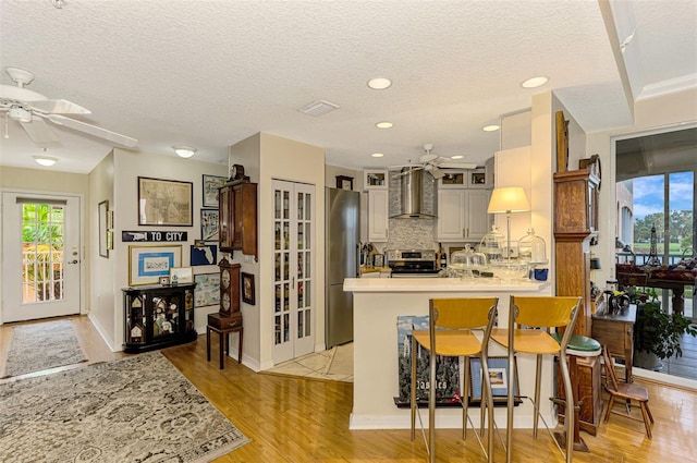 kitchen featuring kitchen peninsula, appliances with stainless steel finishes, a breakfast bar, wall chimney range hood, and light hardwood / wood-style floors