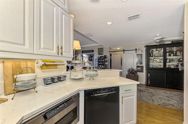 kitchen featuring black dishwasher, a barn door, light hardwood / wood-style floors, a textured ceiling, and white cabinets