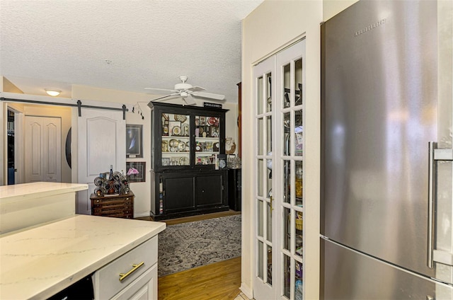 kitchen with light stone counters, high quality fridge, a barn door, light hardwood / wood-style floors, and white cabinetry