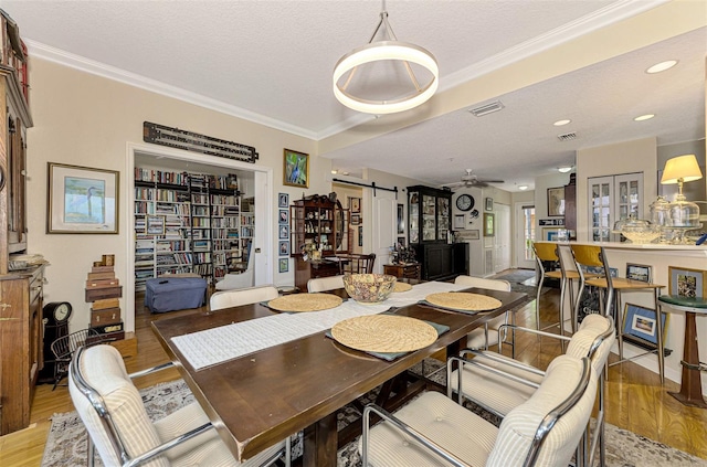 dining area with a barn door, ornamental molding, a textured ceiling, and light wood-type flooring