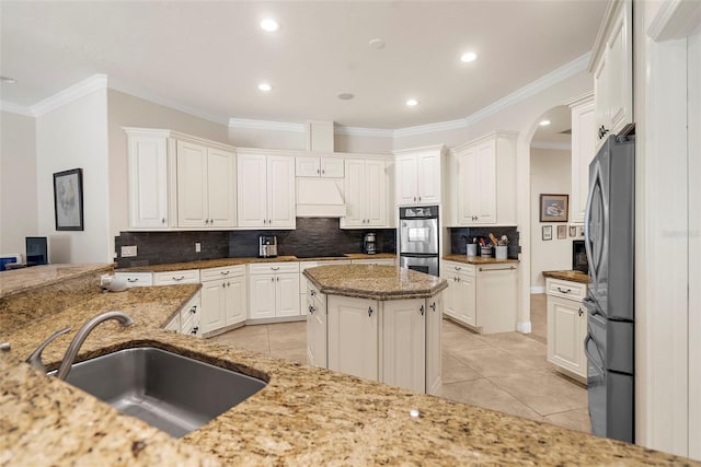 kitchen with light stone counters, stainless steel appliances, sink, light tile patterned floors, and white cabinetry