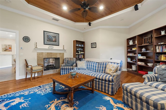 living room featuring ceiling fan, a raised ceiling, wood-type flooring, a tiled fireplace, and wood ceiling