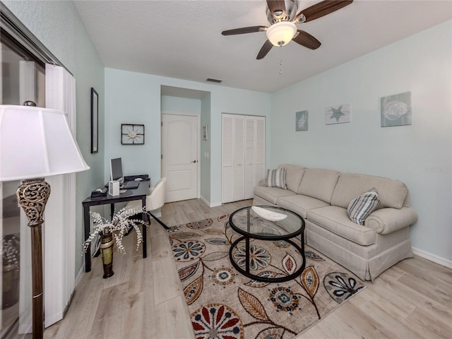 living room with a textured ceiling, light hardwood / wood-style flooring, and ceiling fan