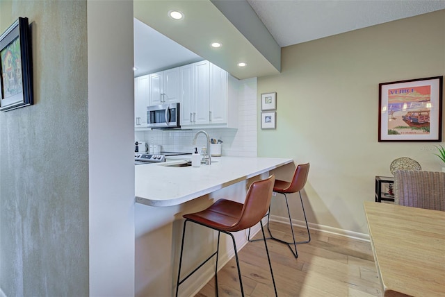 kitchen featuring backsplash, a breakfast bar, sink, light hardwood / wood-style flooring, and white cabinetry