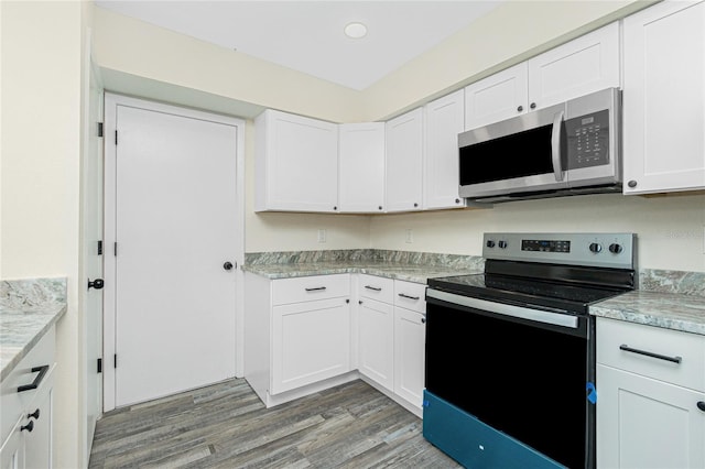 kitchen with hardwood / wood-style flooring, stainless steel appliances, light stone countertops, and white cabinets