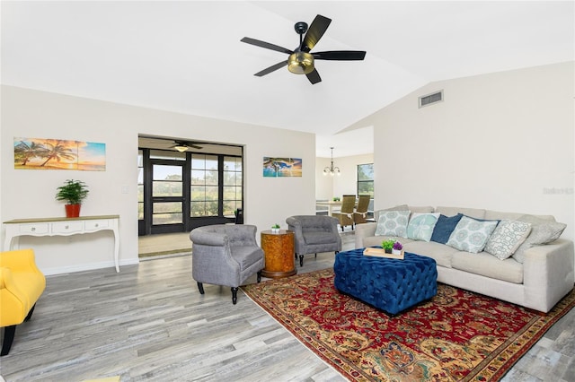 living room with plenty of natural light, ceiling fan with notable chandelier, lofted ceiling, and light wood-type flooring