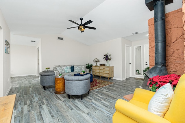 living room with ceiling fan, lofted ceiling, wood-type flooring, and a wood stove