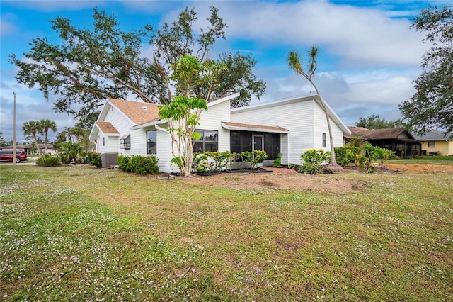 rear view of house featuring a sunroom, central air condition unit, and a lawn