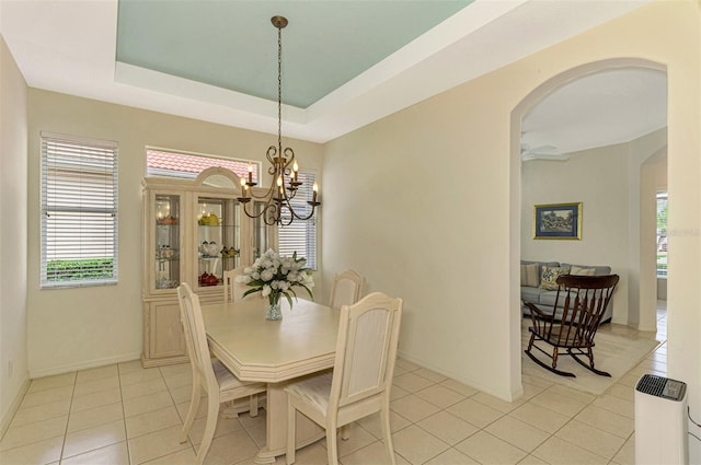 tiled dining area featuring ceiling fan with notable chandelier and a tray ceiling