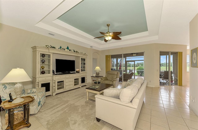 living room with a tray ceiling, ceiling fan, and light tile patterned flooring