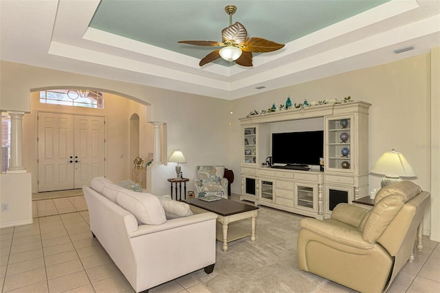 tiled living room with a tray ceiling, ornate columns, and ceiling fan