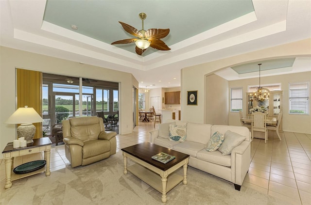 tiled living room with a raised ceiling, plenty of natural light, and ceiling fan with notable chandelier