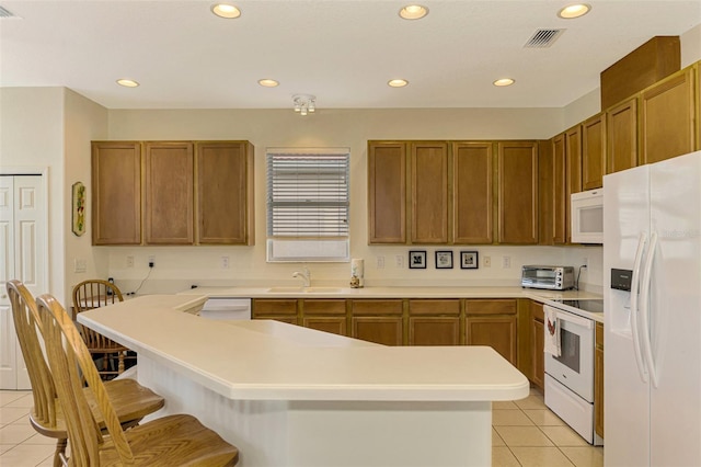 kitchen featuring a breakfast bar, sink, light tile patterned floors, and white appliances