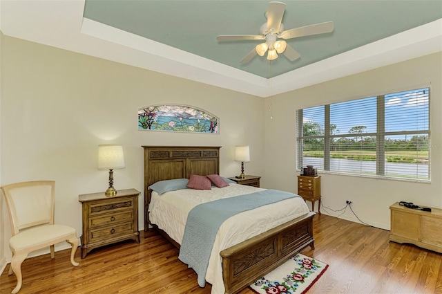 bedroom with ceiling fan, a raised ceiling, and light wood-type flooring