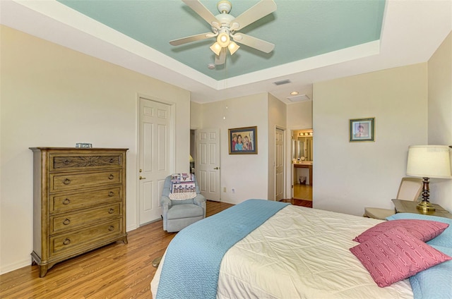 bedroom with a tray ceiling, ensuite bathroom, ceiling fan, and light hardwood / wood-style floors