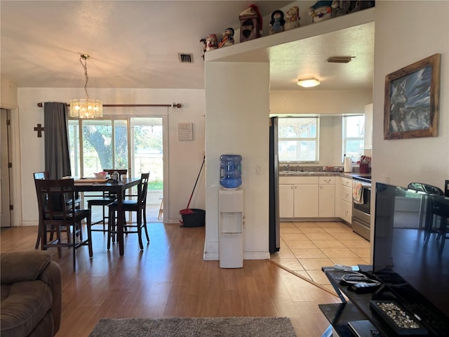 kitchen with white cabinets, hanging light fixtures, light wood-type flooring, stainless steel range oven, and a chandelier