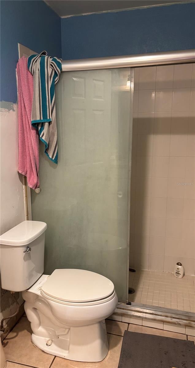 bathroom featuring tile patterned flooring, a shower with door, and toilet