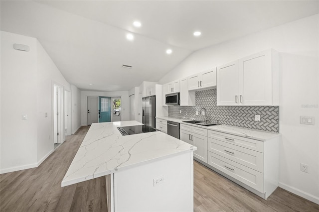 kitchen with a kitchen island, white cabinetry, appliances with stainless steel finishes, and vaulted ceiling