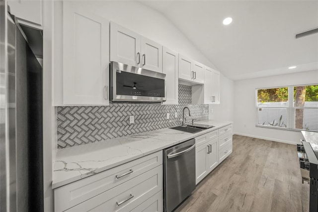 kitchen featuring light stone countertops, stainless steel appliances, vaulted ceiling, sink, and white cabinetry