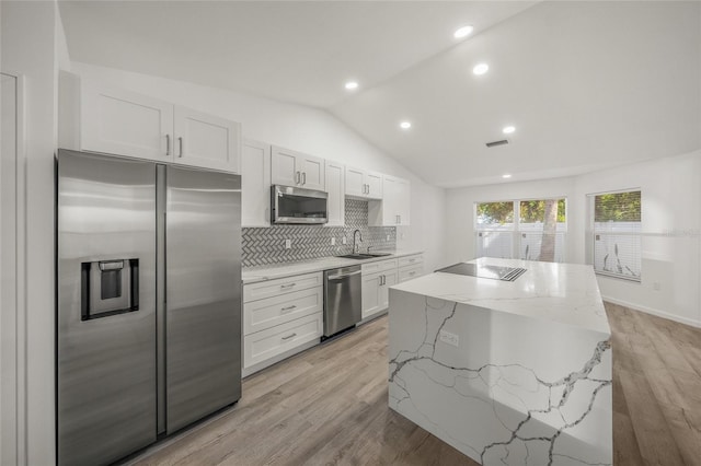 kitchen with appliances with stainless steel finishes, light stone counters, sink, white cabinets, and light hardwood / wood-style floors