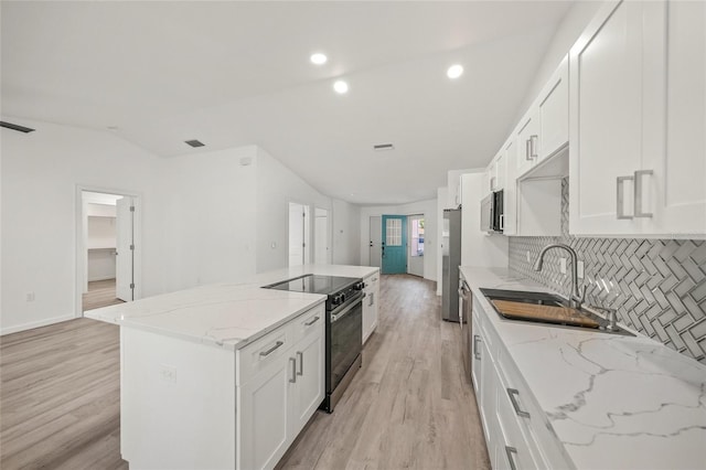 kitchen featuring appliances with stainless steel finishes, white cabinetry, light stone counters, a kitchen island, and light wood-type flooring