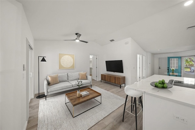 living room featuring ceiling fan, light hardwood / wood-style floors, and vaulted ceiling