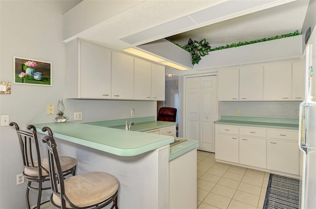 kitchen with white cabinets, white refrigerator, a kitchen bar, and kitchen peninsula