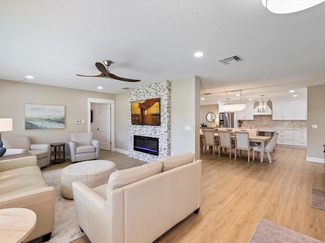 living room with ceiling fan, a large fireplace, and light hardwood / wood-style flooring