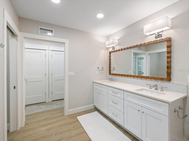 bathroom featuring hardwood / wood-style flooring, vanity, a textured ceiling, and tasteful backsplash