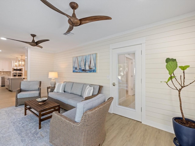 living room featuring light hardwood / wood-style floors, ceiling fan, and wooden walls