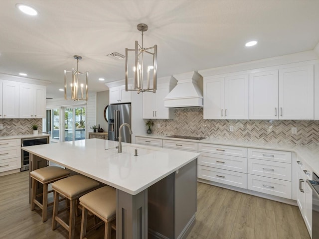 kitchen featuring beverage cooler, decorative light fixtures, a kitchen island with sink, high end fridge, and custom range hood