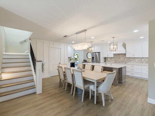 dining space with a notable chandelier, sink, a textured ceiling, and light hardwood / wood-style flooring