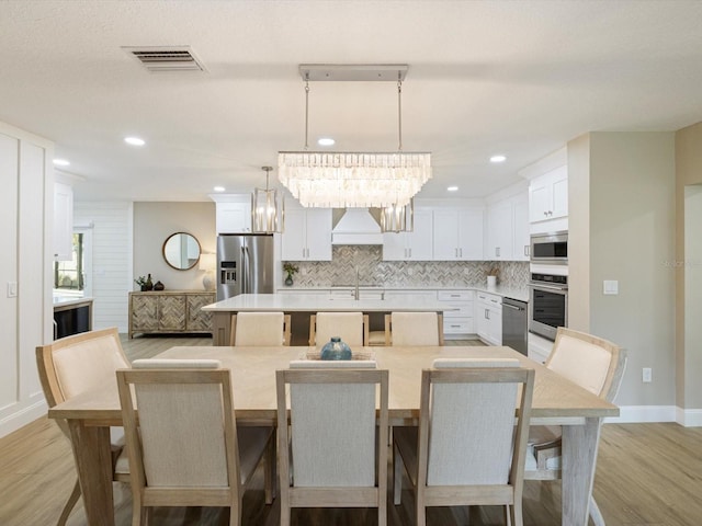 dining area with sink, light wood-type flooring, and a notable chandelier