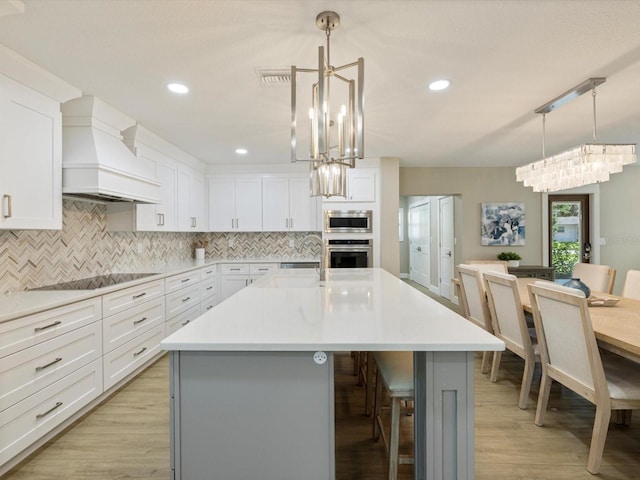 kitchen with premium range hood, a center island with sink, light wood-type flooring, and appliances with stainless steel finishes