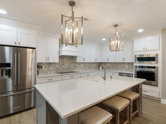 kitchen featuring stainless steel appliances, a kitchen island with sink, sink, pendant lighting, and light hardwood / wood-style flooring