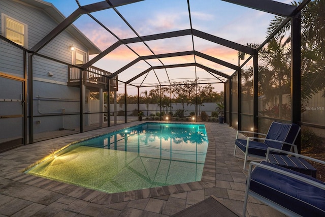 pool at dusk with glass enclosure, a patio area, and a fenced in pool