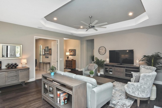 living room featuring a raised ceiling, ceiling fan, and dark wood-type flooring