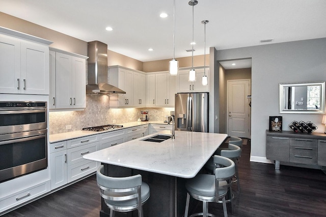 kitchen featuring pendant lighting, sink, wall chimney exhaust hood, appliances with stainless steel finishes, and white cabinetry