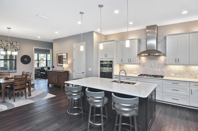 kitchen featuring sink, wall chimney range hood, dark hardwood / wood-style flooring, an island with sink, and decorative light fixtures