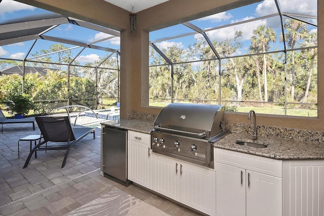 view of patio with sink, glass enclosure, grilling area, and exterior kitchen