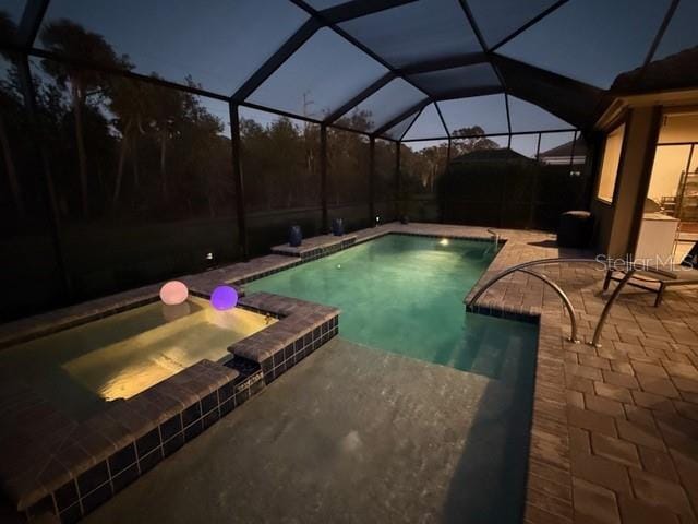 pool at dusk with a lanai, a patio area, and an in ground hot tub