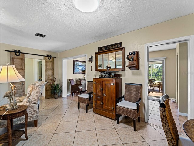 living area with a textured ceiling, a barn door, and light tile patterned flooring