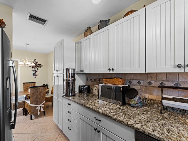 kitchen featuring tasteful backsplash, dark stone counters, light tile patterned floors, a notable chandelier, and hanging light fixtures