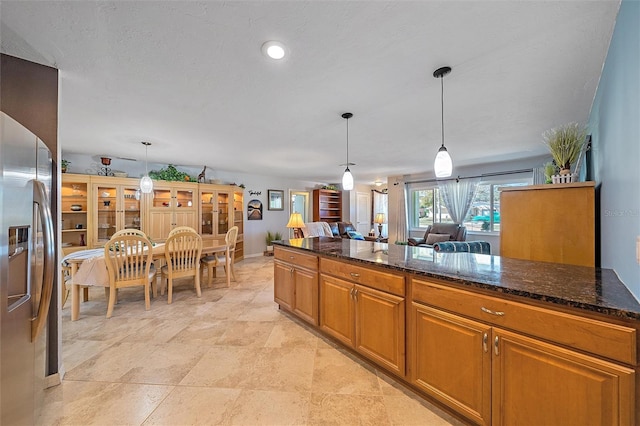 kitchen featuring pendant lighting, stainless steel refrigerator with ice dispenser, dark stone counters, and a textured ceiling