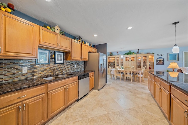 kitchen with tasteful backsplash, dark stone counters, stainless steel appliances, sink, and decorative light fixtures