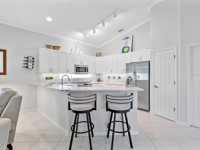 kitchen featuring kitchen peninsula, appliances with stainless steel finishes, a kitchen breakfast bar, light stone counters, and white cabinetry